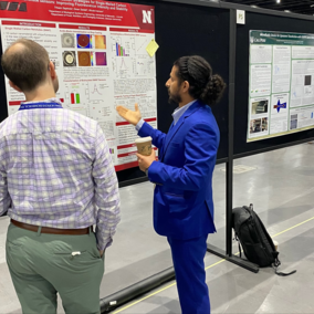 Two people discussing a scientific poster at a conference, one gesturing while holding a coffee cup.