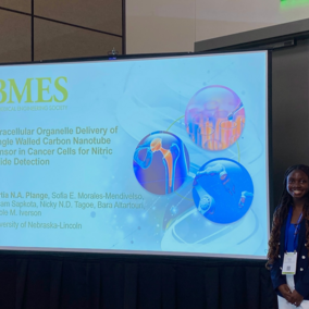 Presentation slide with research title and graphics alongside a person standing nearby.